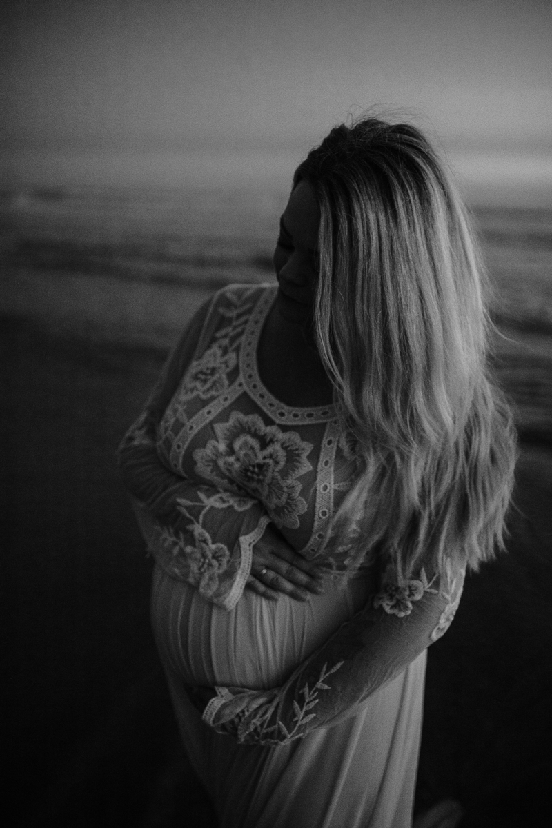 Temecula Maternity Photographer, black and white image of mother holding her belly at the beach
