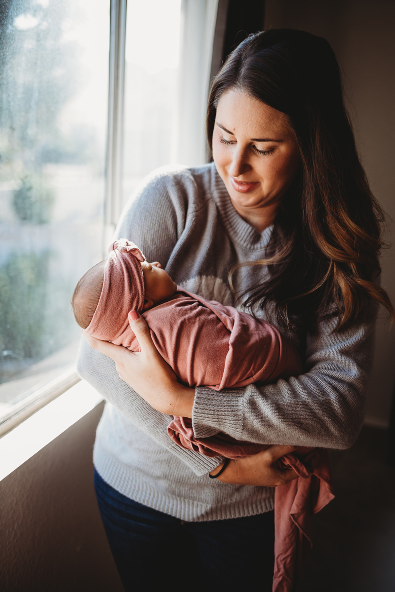 Temecula Newborn Photographer, mother holding baby girl next to a window