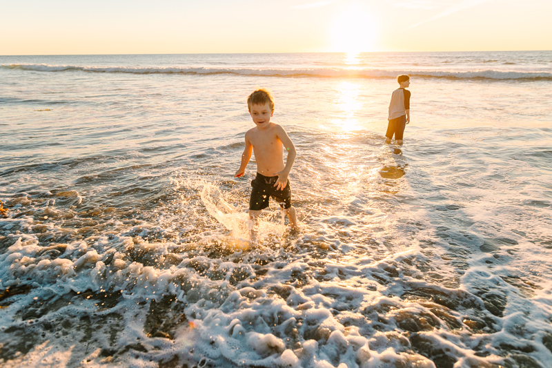 Family Photographer, two young children play in quiet ocean tides at sunset