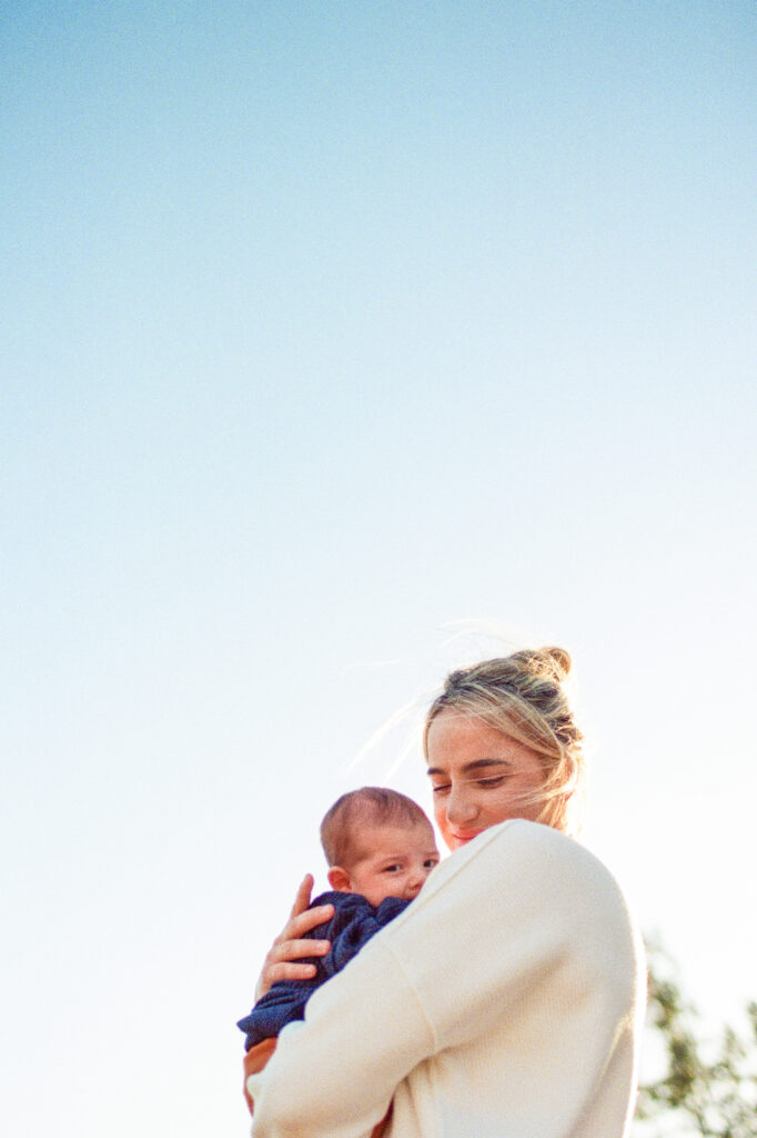 Family Photographer, a mother holds her newborn baby before a clear blue sky